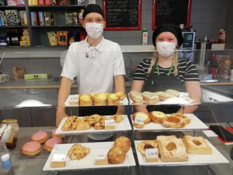 Kesäkoululaiset seisovat kahvilan tiskin takana